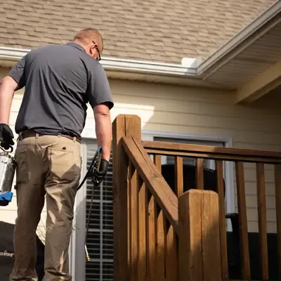 pest technician spraying exterior of home